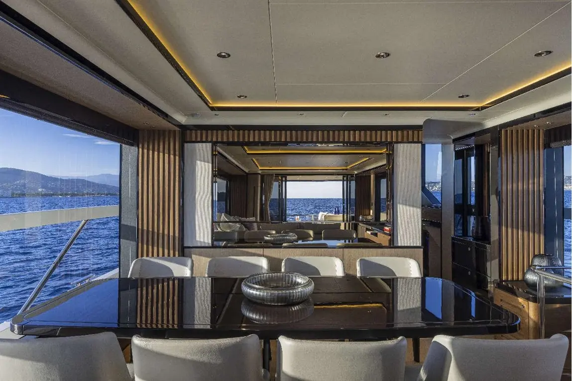 Luxurious yacht interior with a black glass dining table, soft chairs, and views of the sea through large windows.